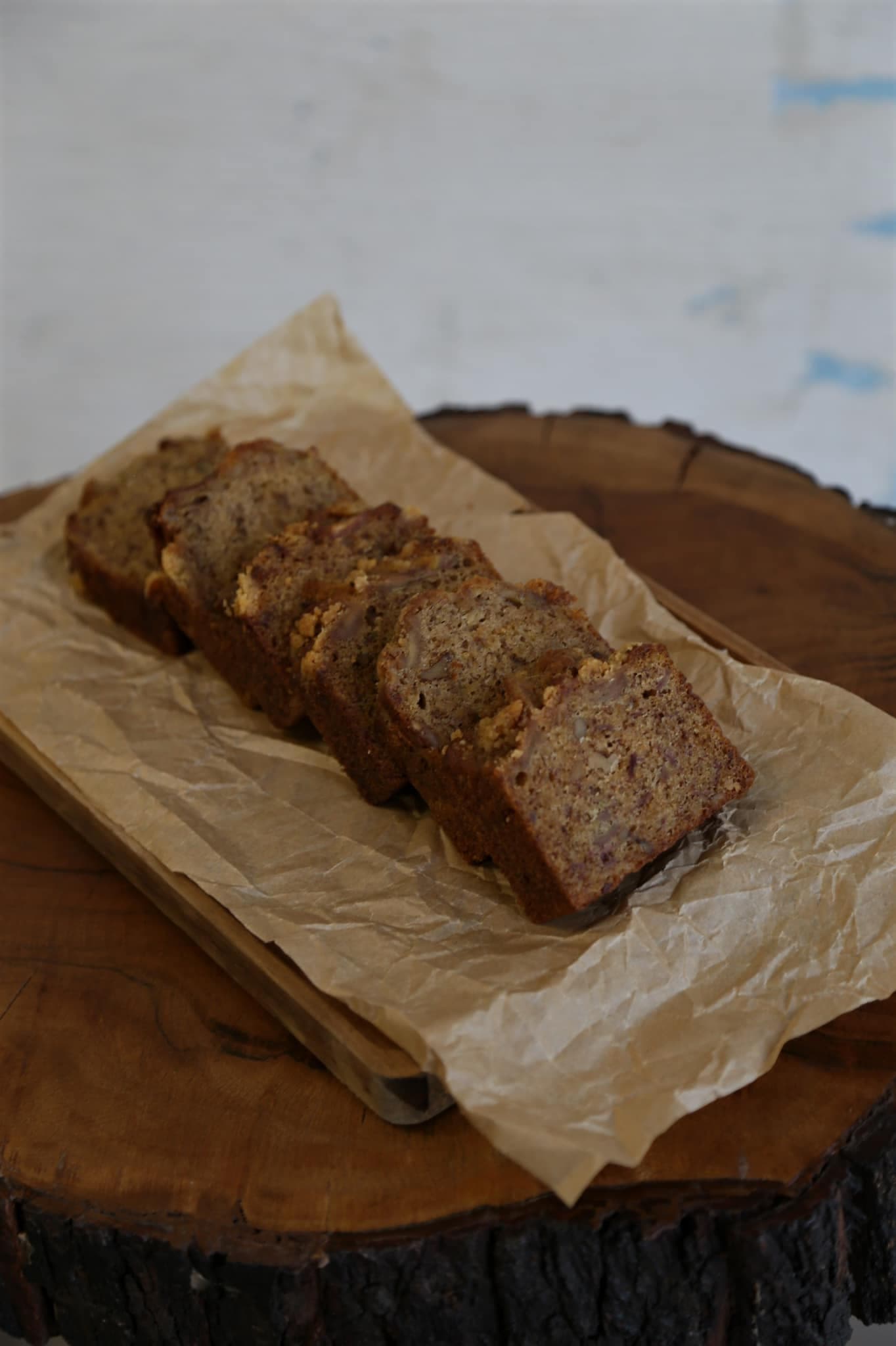 Slices of moist banana bread arranged on parchment paper over a rustic wooden board.