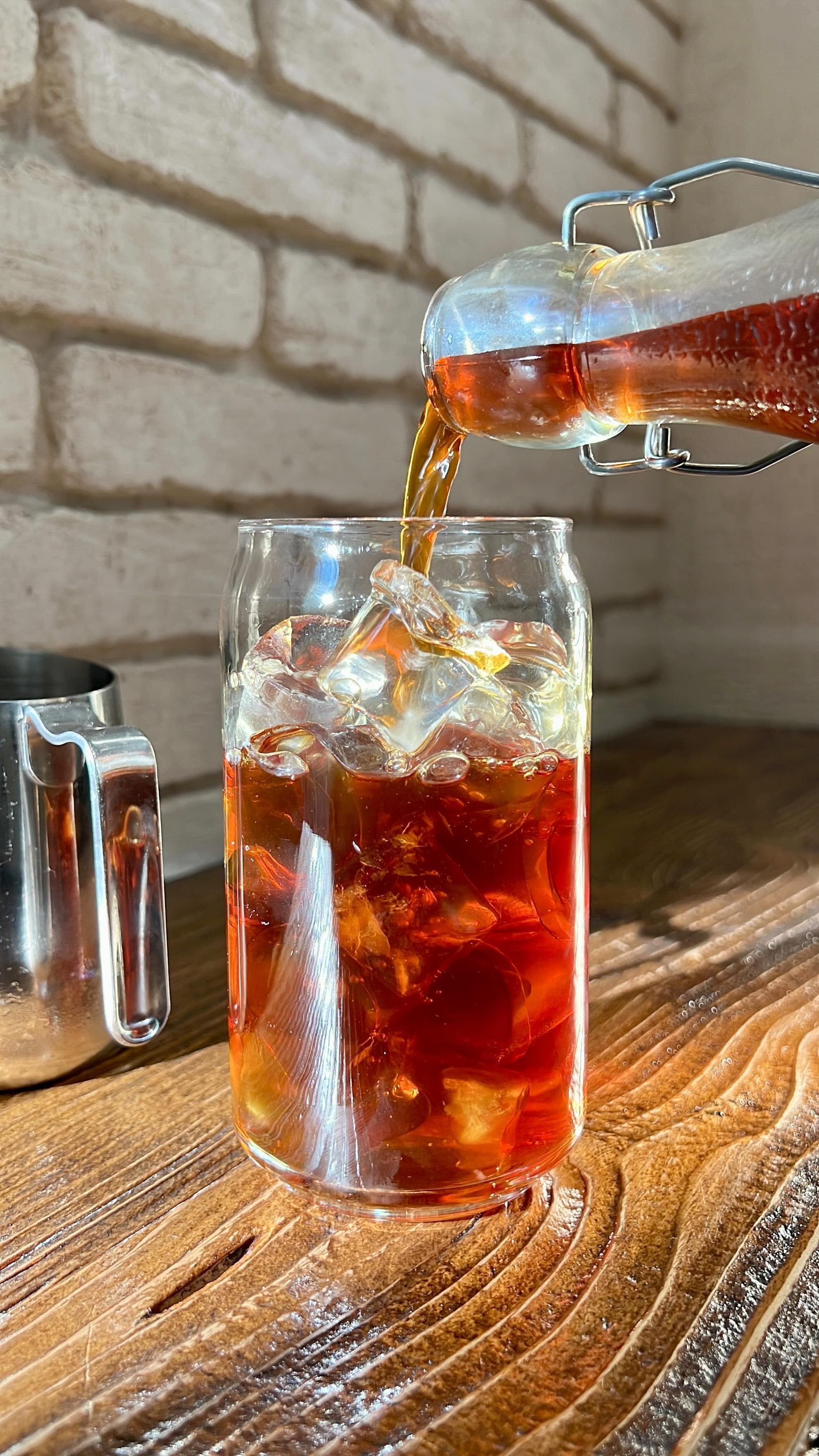 Dark amber liquid pouring from a bottle into a glass filled with ice cubes.