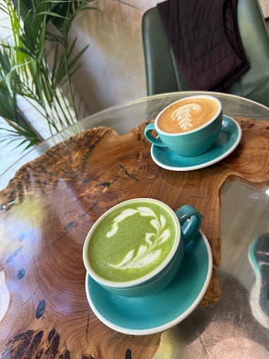 Green matcha and brown coffee lattes with leaf foam art on a wooden table.