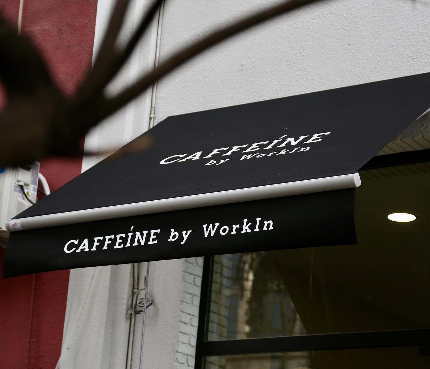 Black awning with white text 'CAFFEINE by WorkIn' attached to a white building exterior.