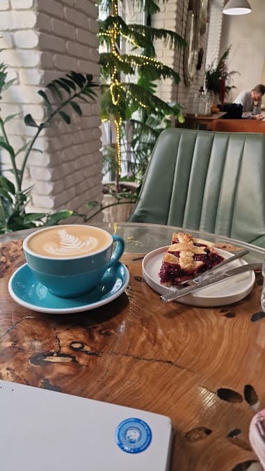 Blue cup of latte with leaf art and cherry pie on a polished wooden table.