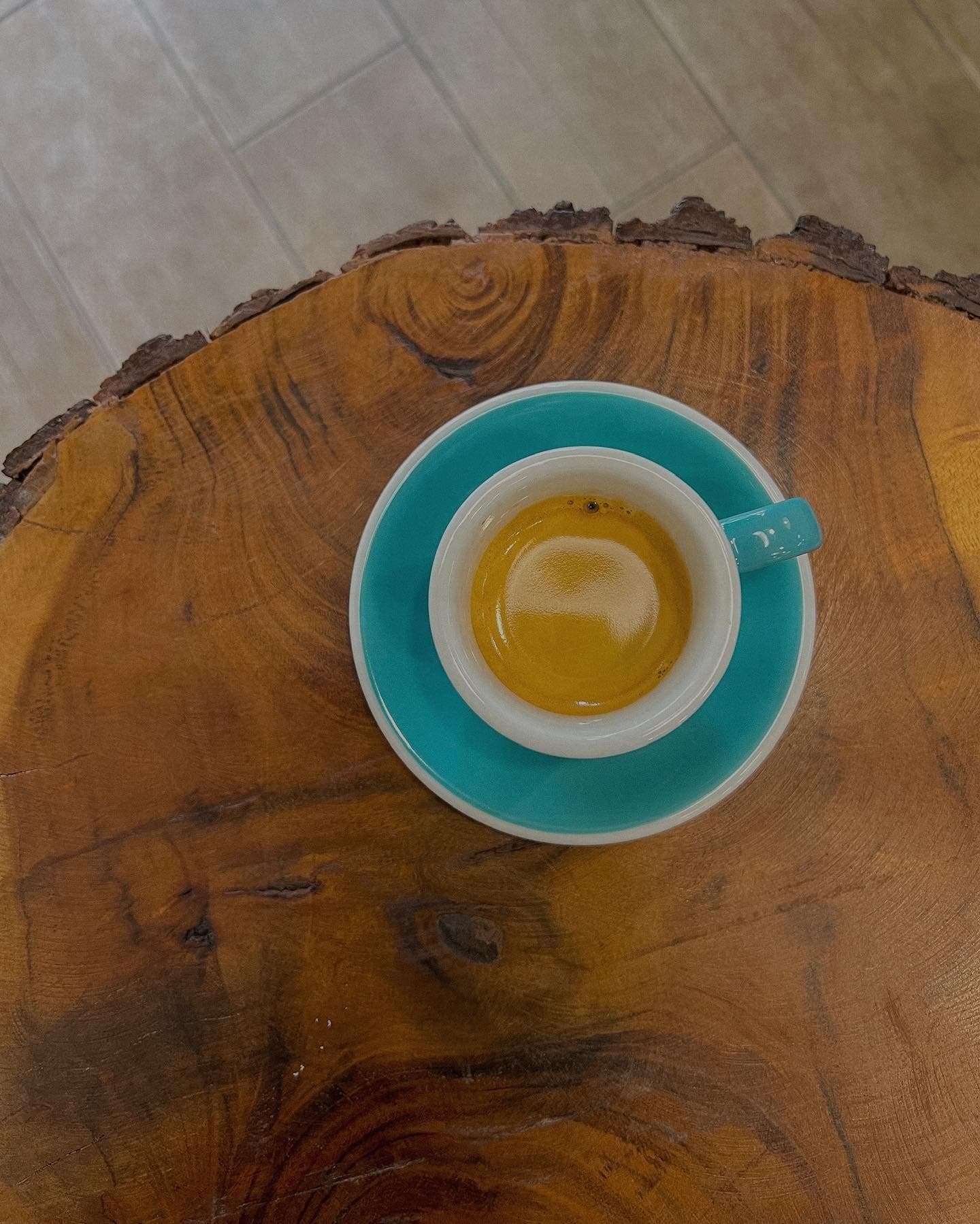 Espresso in a white cup and teal saucer on a rustic, live-edge wooden table.