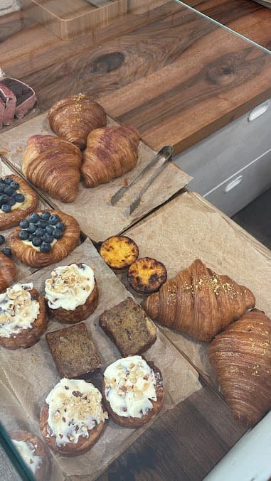 Freshly baked croissants, blueberry tarts, and frosted pastries displayed on a wooden bakery counter.