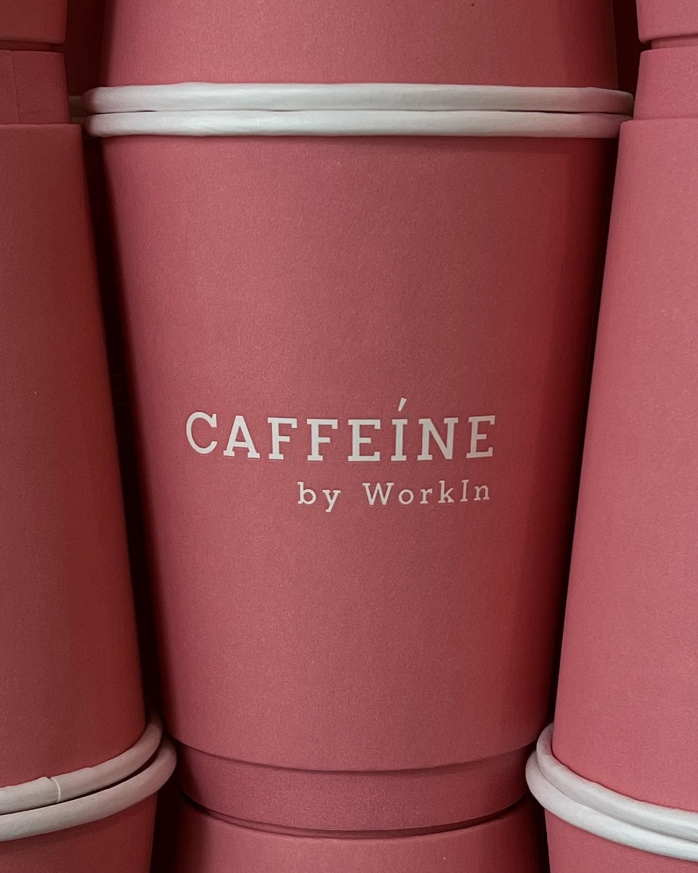 Stacked pink paper cups with white rims and white text reading CAFFEINE by WorkIn.