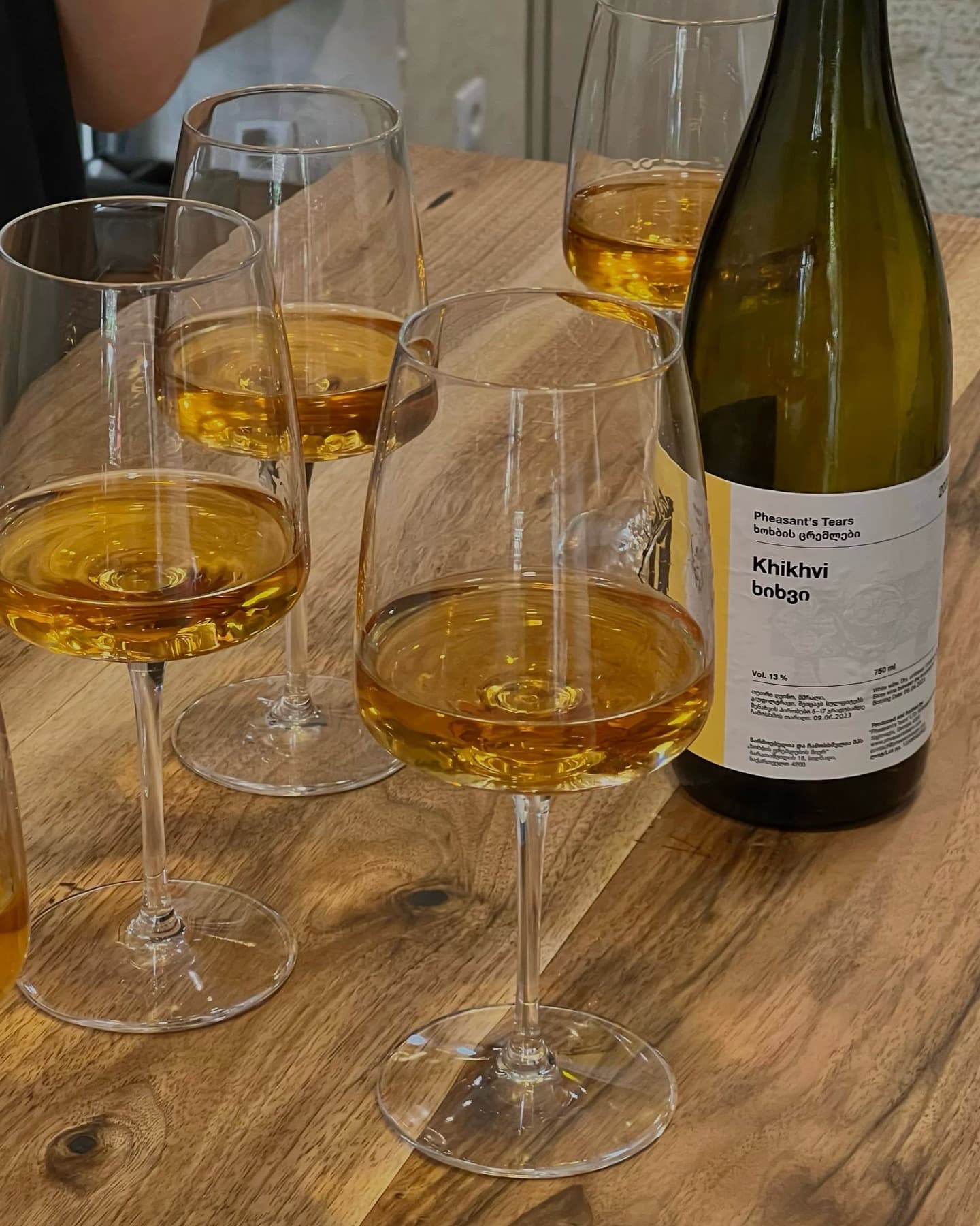 Four glasses of amber wine and a bottle of Pheasant's Tears Khikhvi on wood.