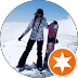 Snowboarder in winter gear posing with a purple snowboard on a snowy mountain peak.